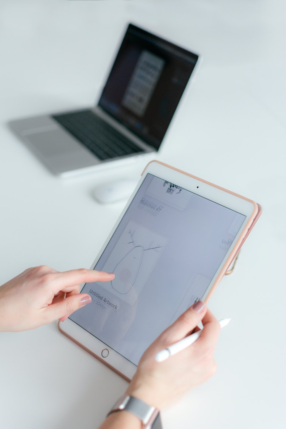 Ruce používající tablet a stylus na bílém stole.